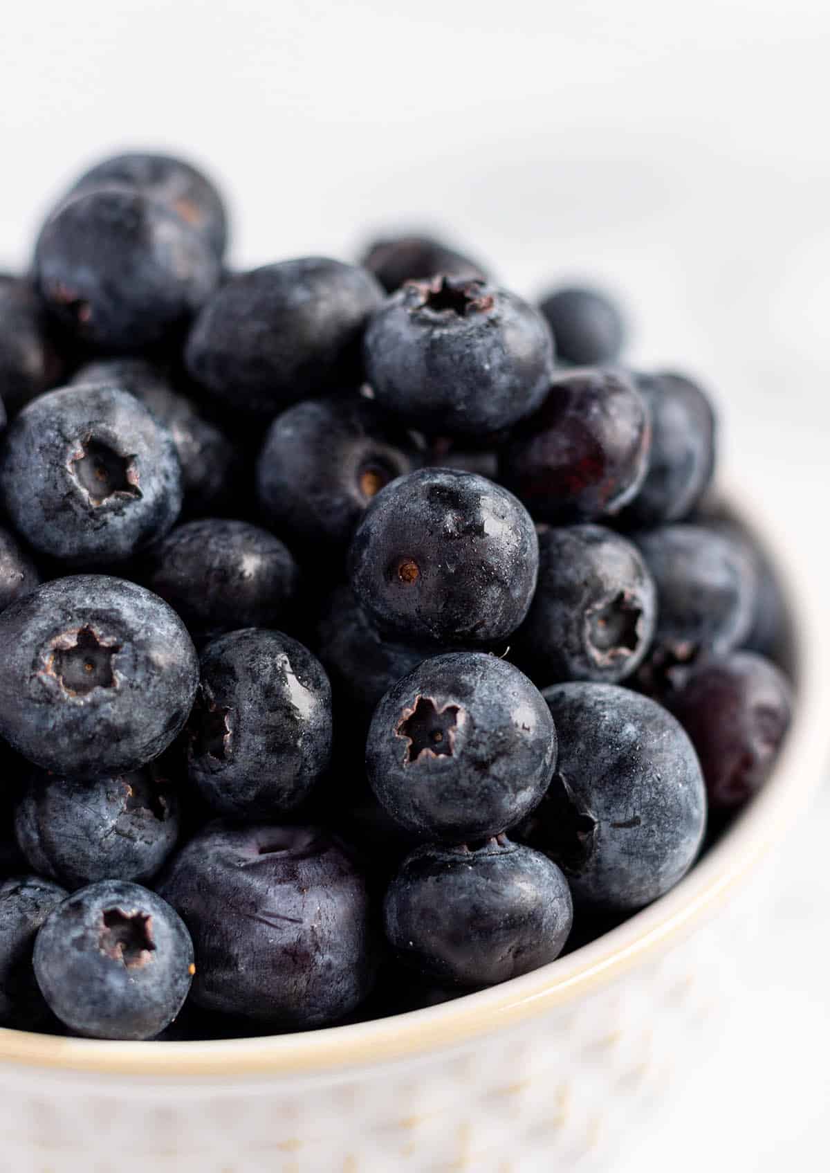 A white bowl with a pile of fresh blueberries