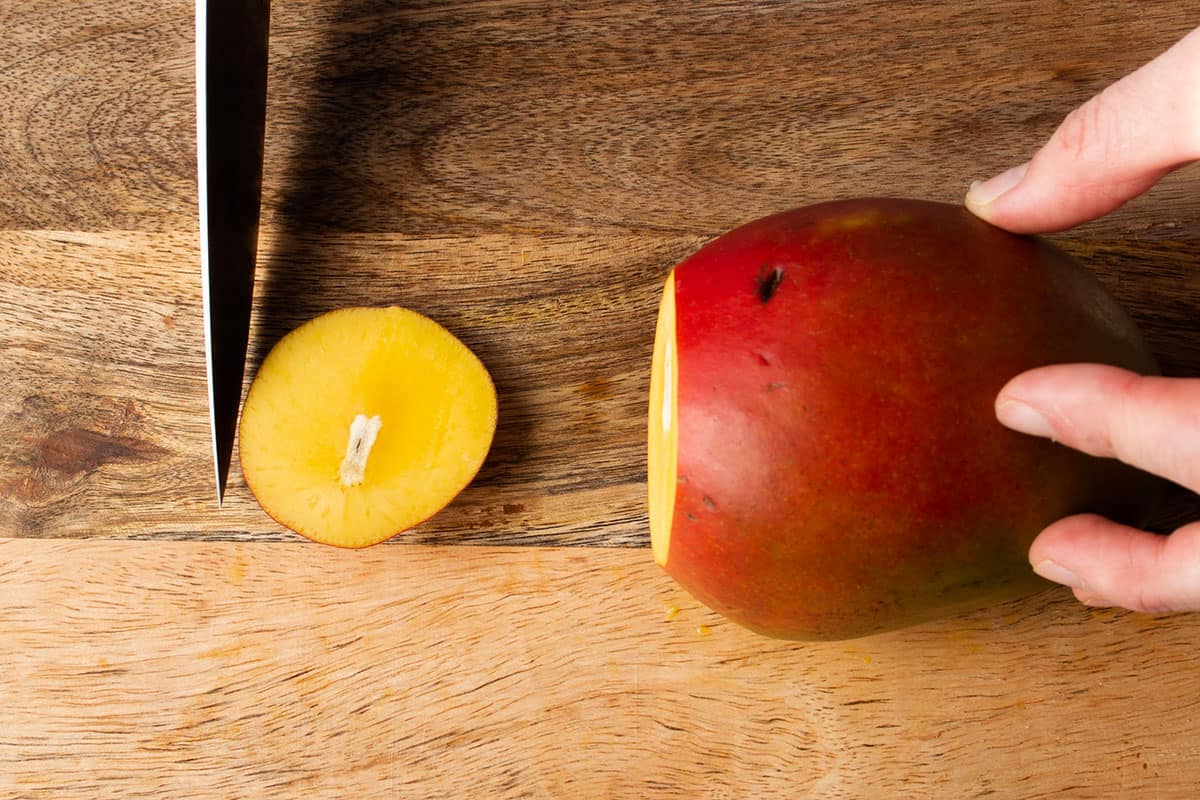A knife cutting off the bottom piece of a mango.