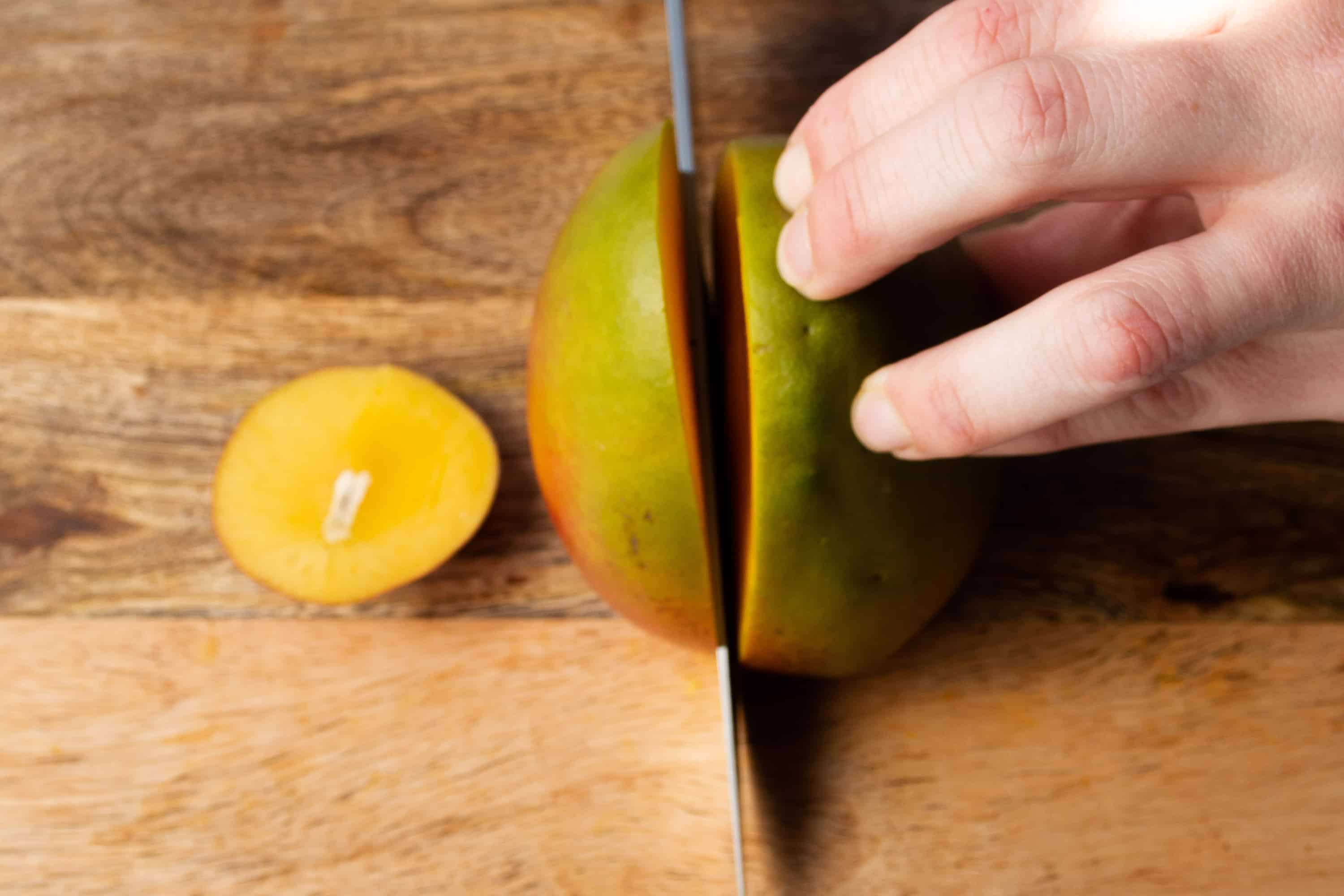 A sharp knife cutting into the top of a mango.