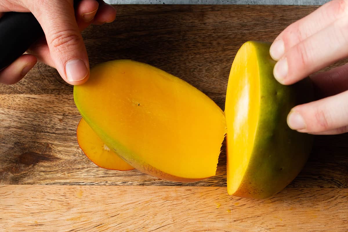 A mango with the first side being cut off from the pit.