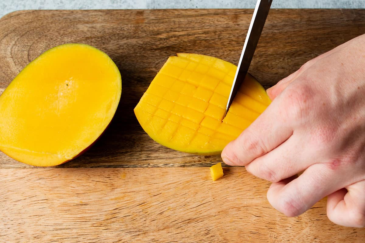 A knife cutting a crosshatch pattern in a mango.