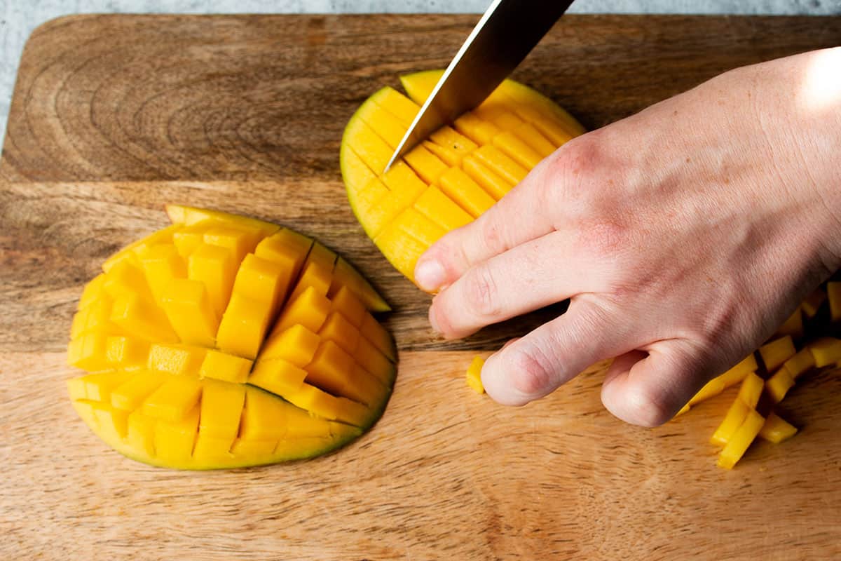 Two pieces of mango and a knife cutting a crosshatch pattern.