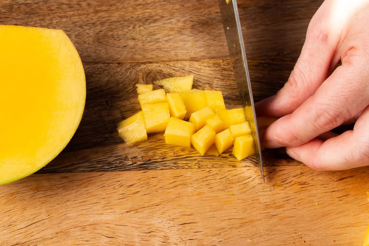 A knife cutting up a small piece of mango into bite size pieces.