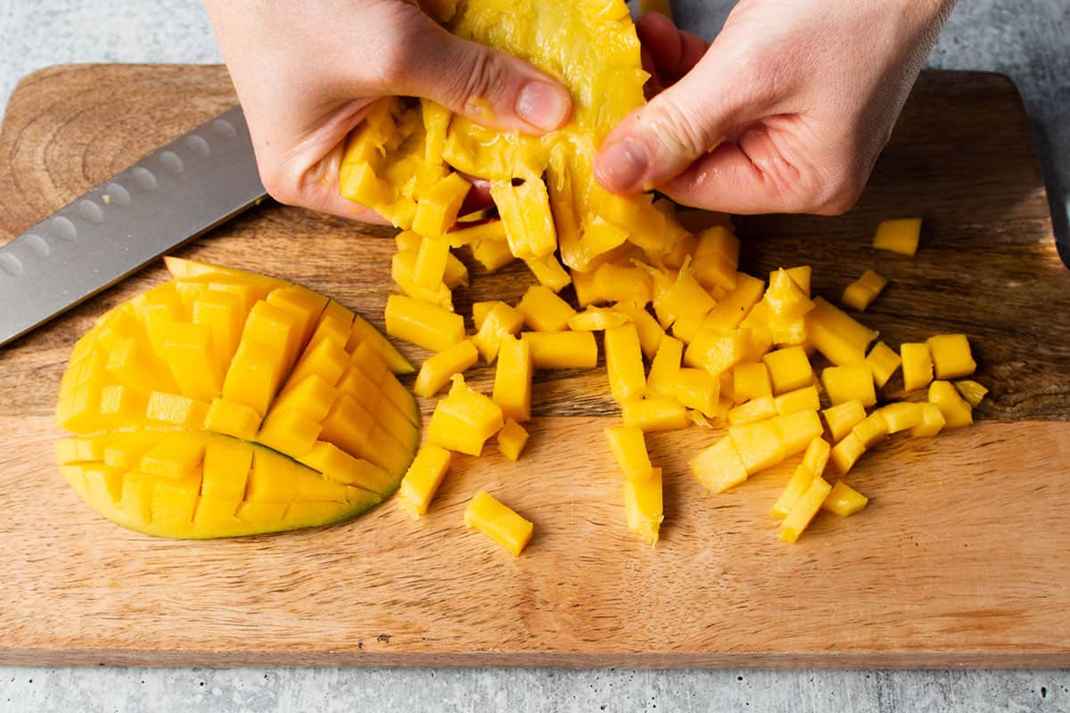 Two hands removing the diced mango from the skin.