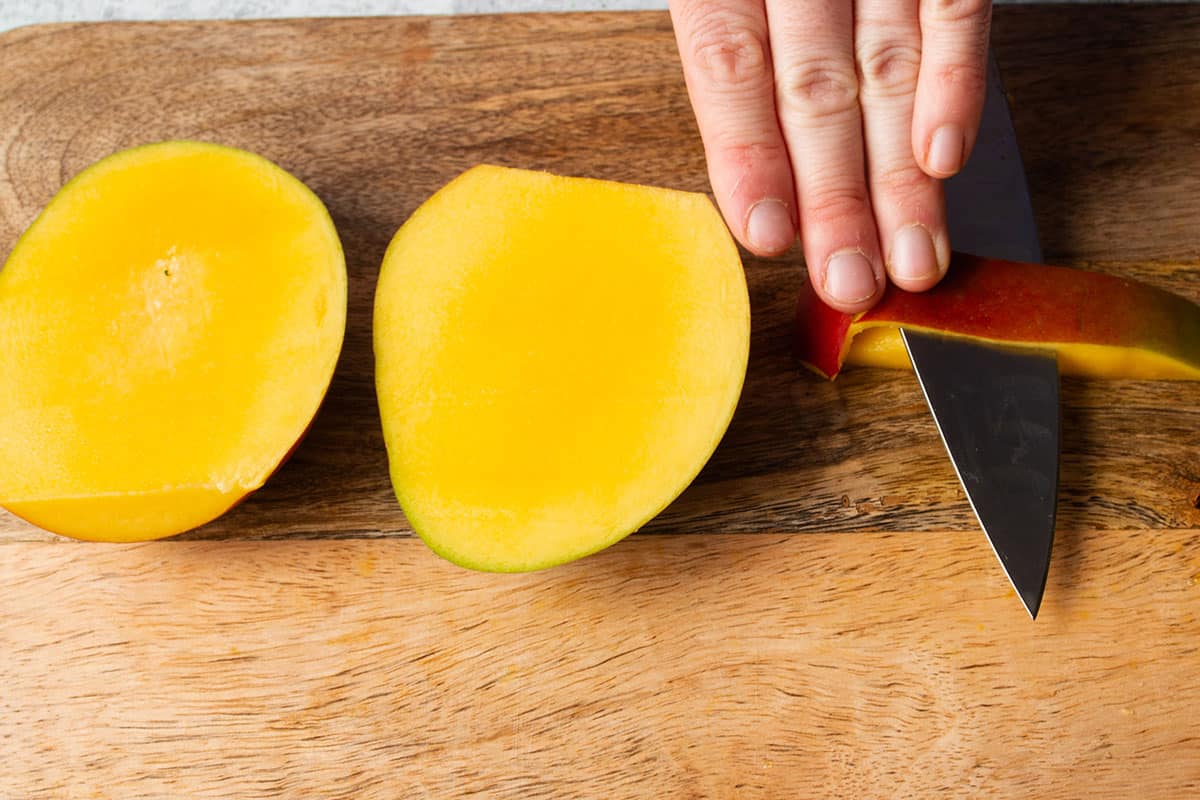 A knife cutting away the skin from a small piece of mango. 