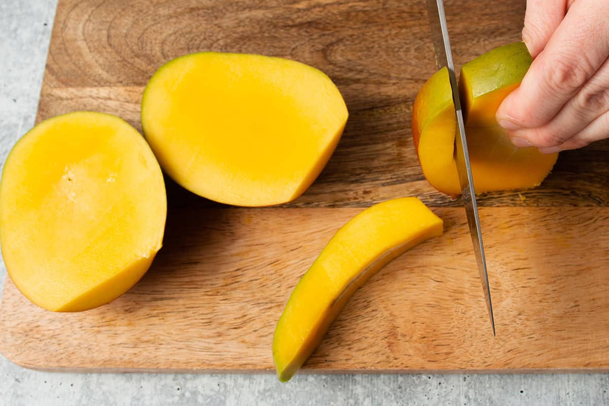 A mango with 3 pieces already removed and the last side being cut off.