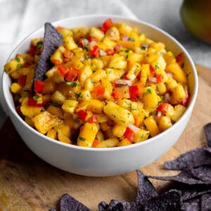 A bowl with diced mangos, pineapples and blue corn tortilla chips on a wooden board.