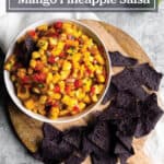 Wooden board with a bowl of mango pineapple salsa and blue corn tortilla chips.
