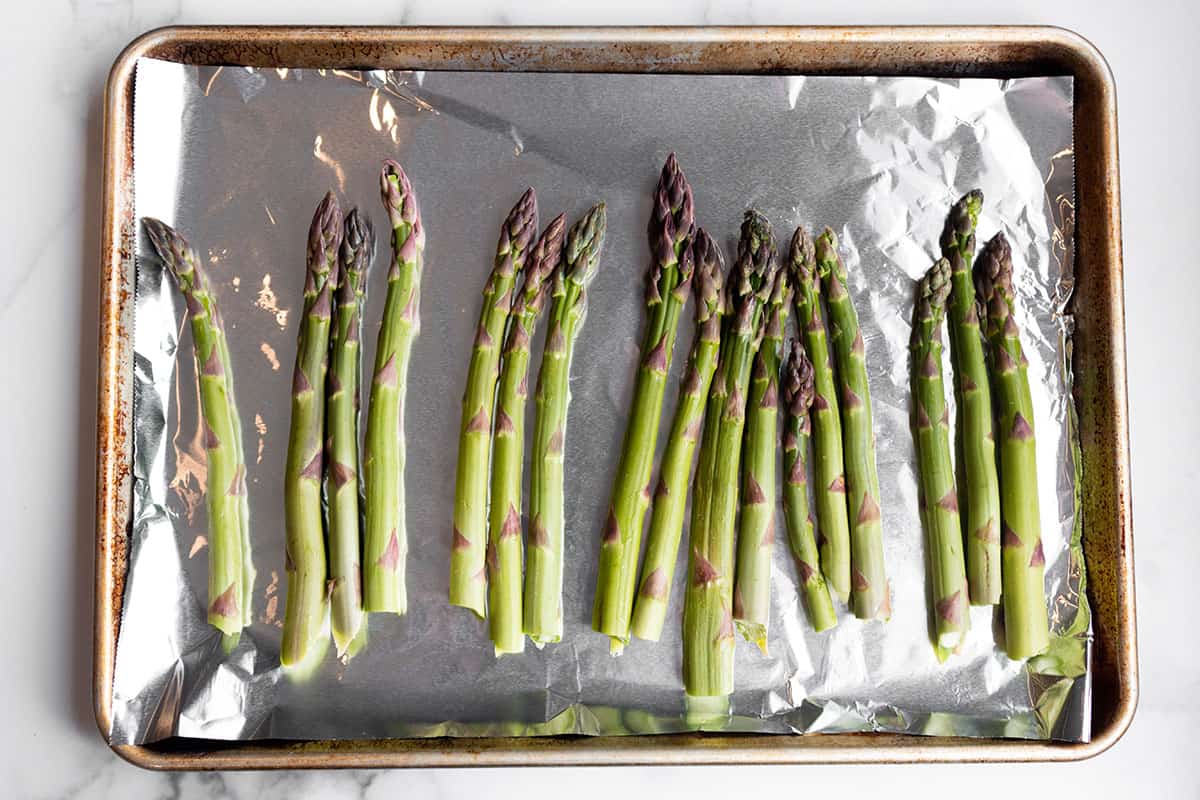 A rimmed baking sheet with aluminum foil and a single layer of asparagus.