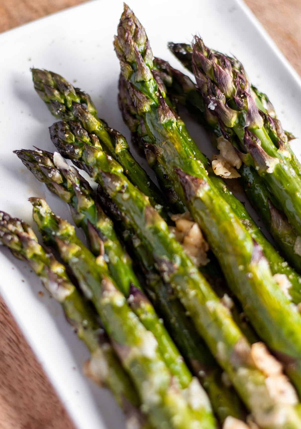 White plate with a stack of oven-roasted asparagus with flakes of parmesan cheese.
