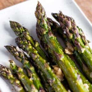 A white plate with roasted asparagus stalks.