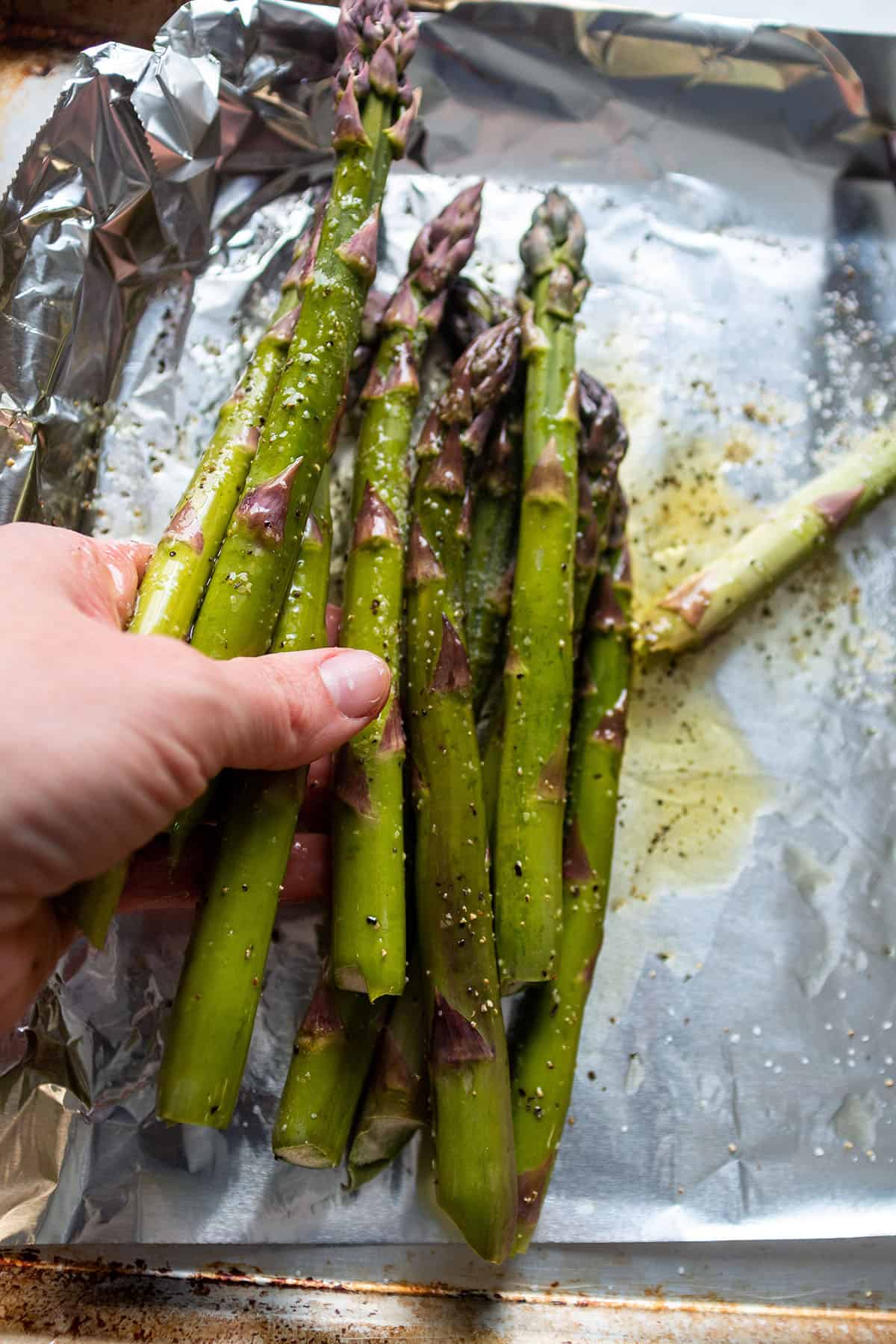A hand tossing asparagus to evenly coat it with the olive oil, salt and pepper.