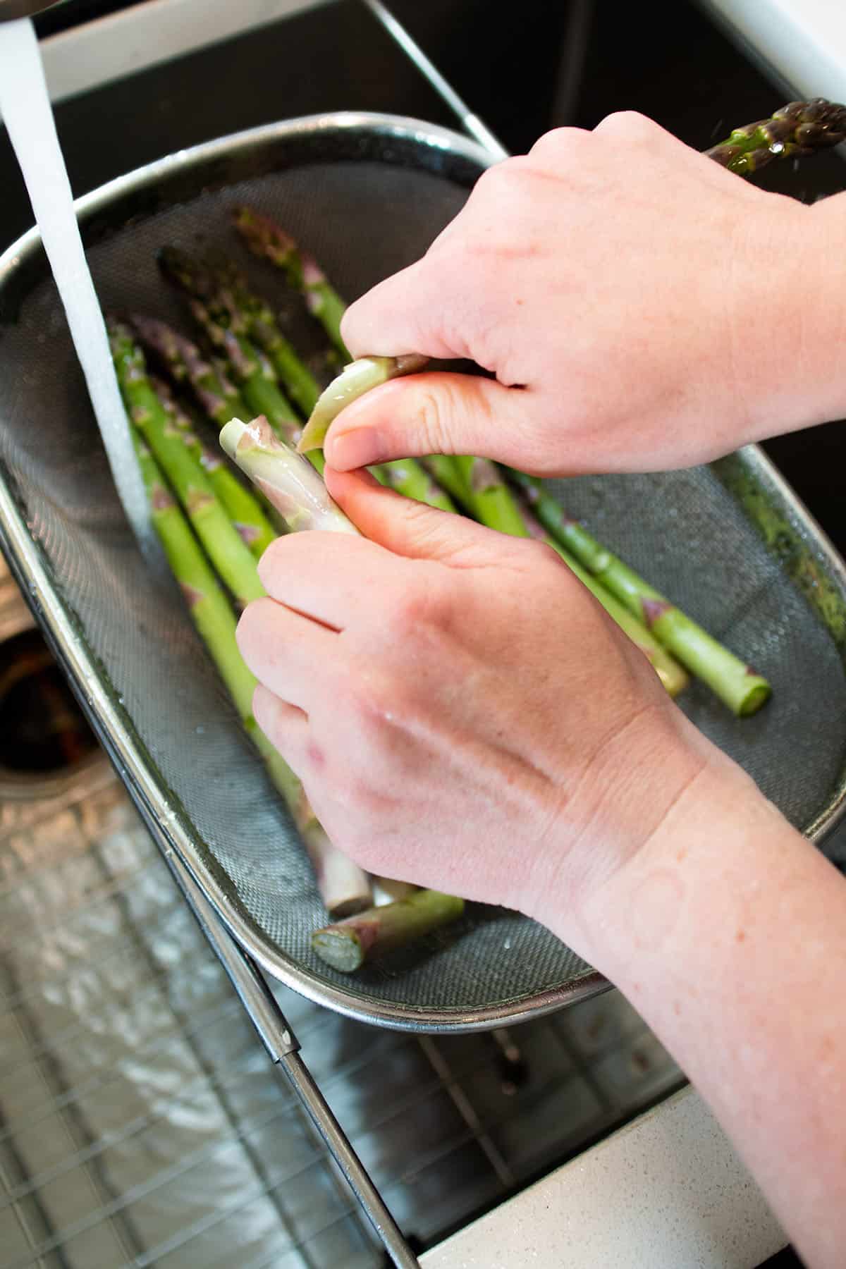 Two hands holding a stalk of asparagus and snapping off the woody bottom.