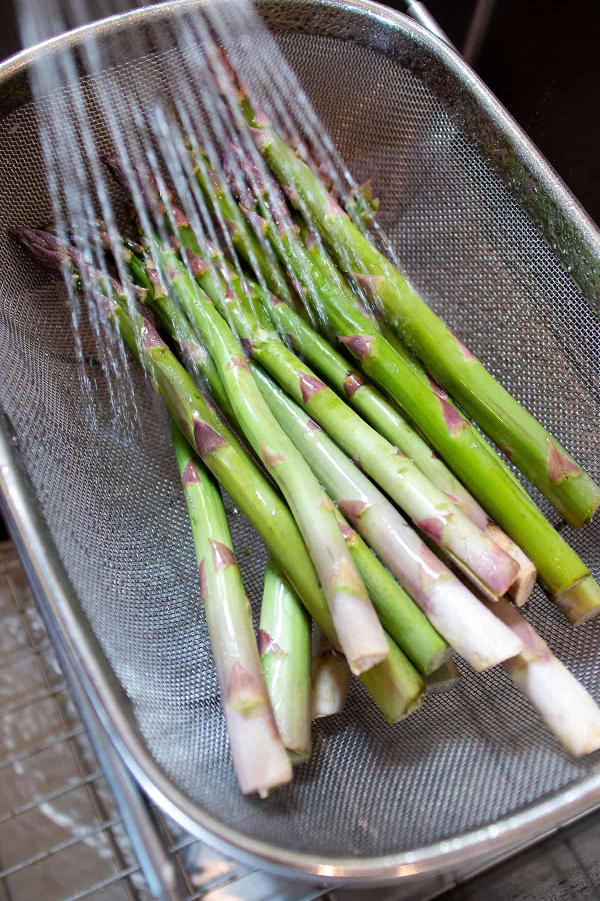 A colander with fresh asparagus being rinsed. 