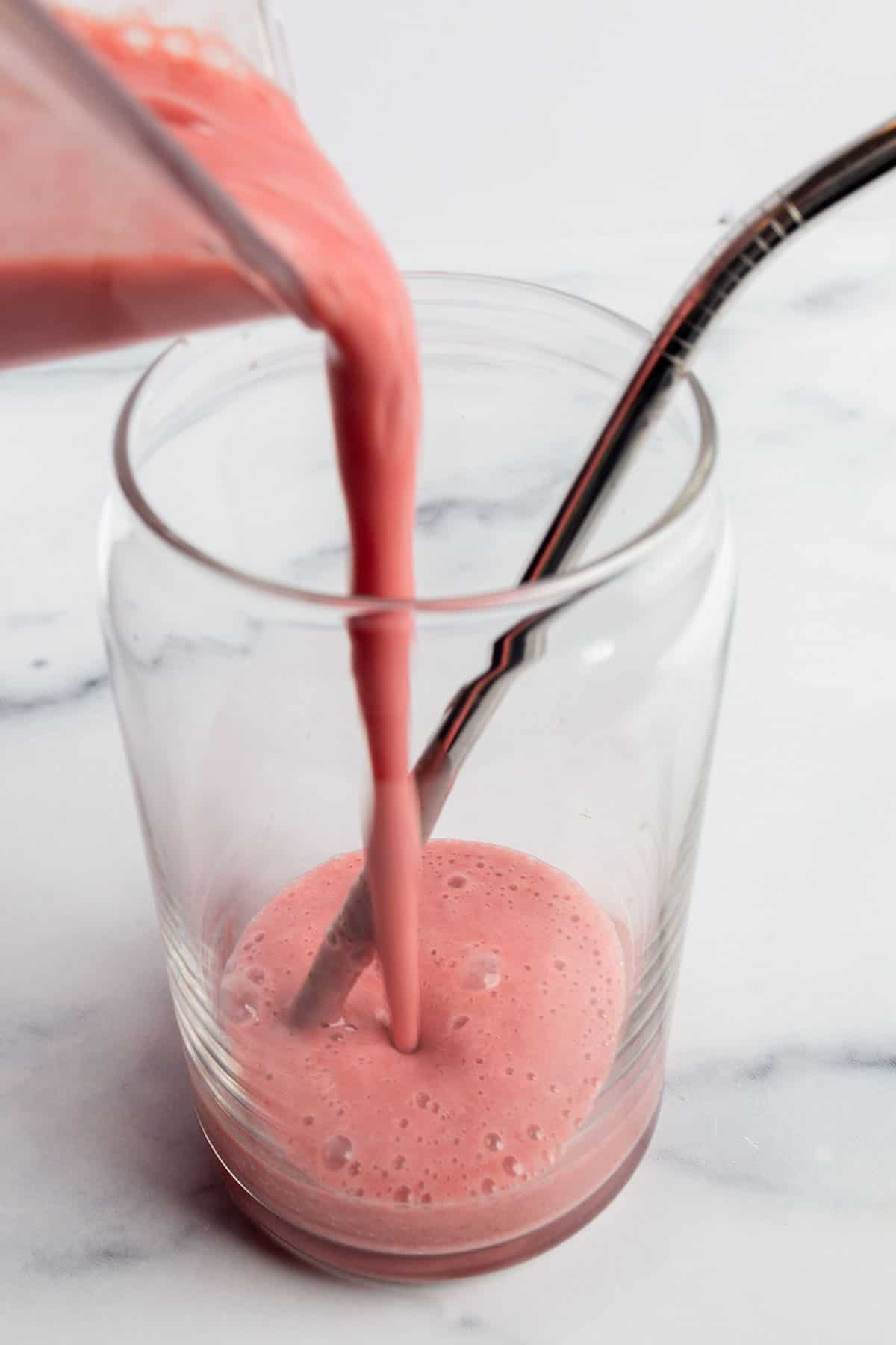 A glass with metal straw with a strawberry rhubarb smoothie being poured in.