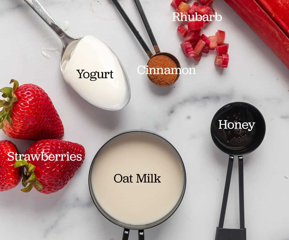 Ingredients for a smoothie. Rhubarb, strawberries, yogurt, oat milk, honey, cinnamon, and strawberries.