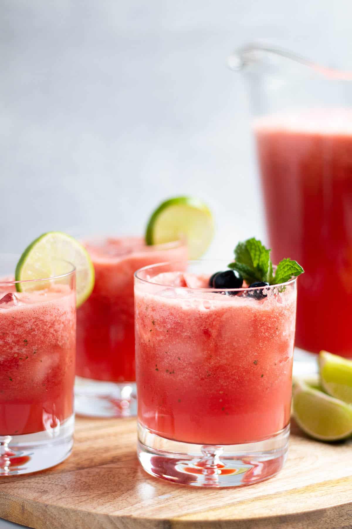 Three small glasses filled with watermelon limeade with fresh limes and mint leaves. 