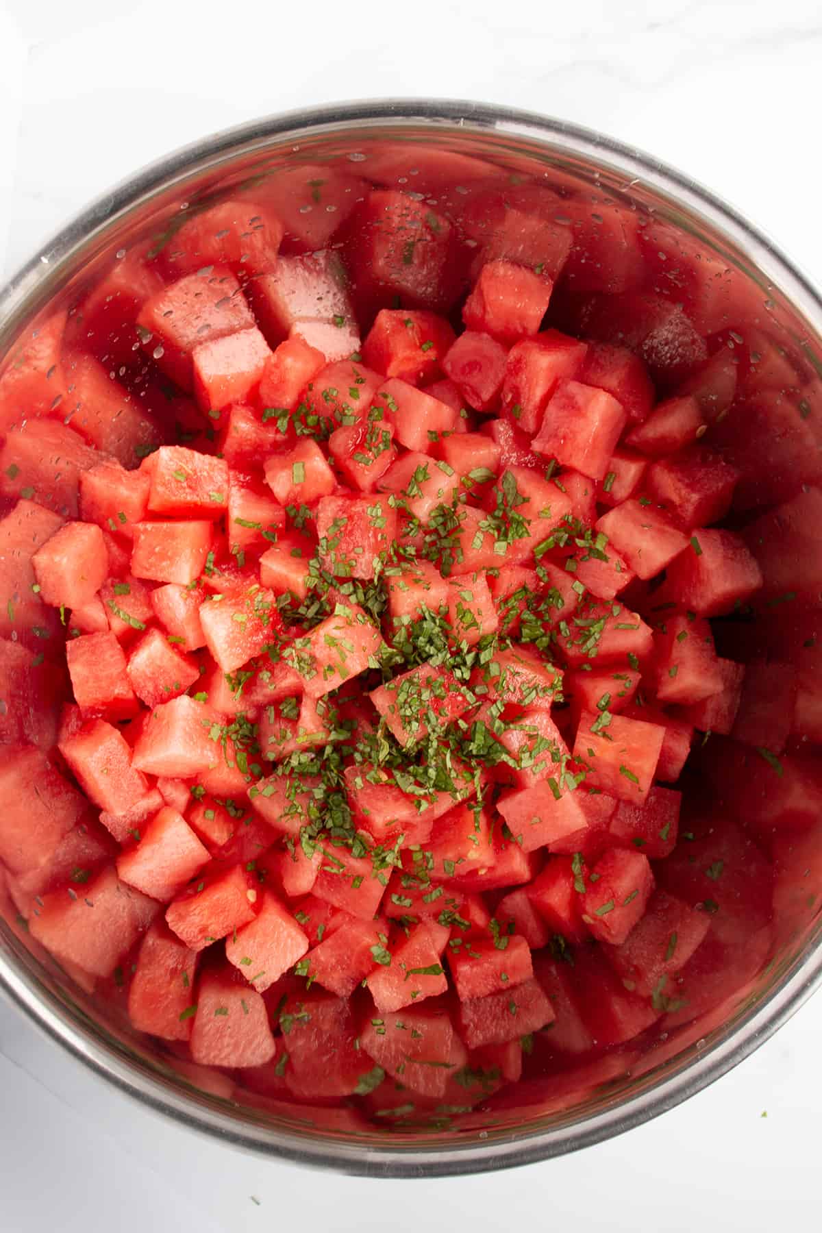 Large metal bowl with diced watermelon and freshly cut mint.