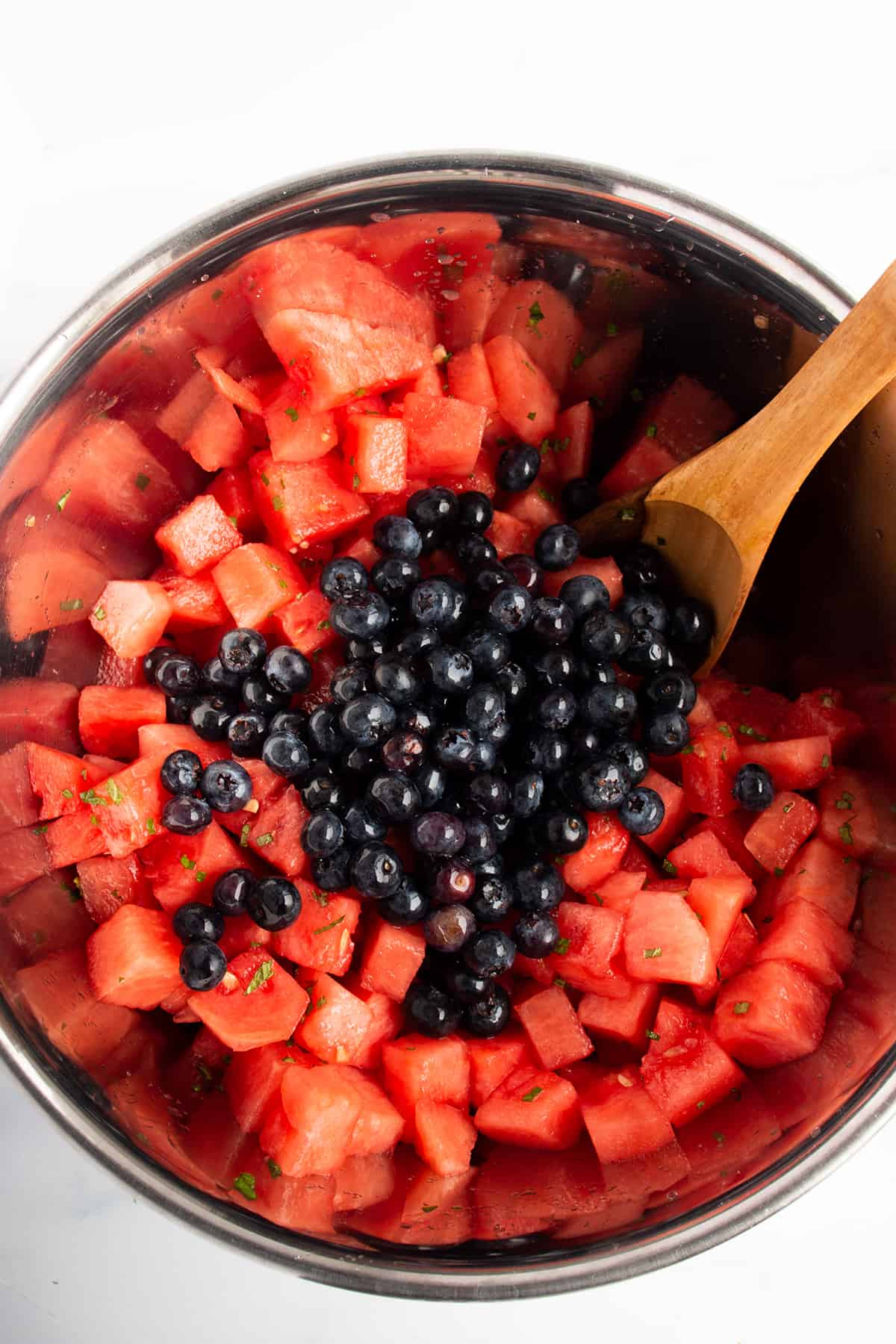 Metal bowl with diced watermelon and fresh blueberries on top with a wooden spoon.