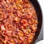 A cast iron pan with a baked bean dish topped with crispy bacon.
