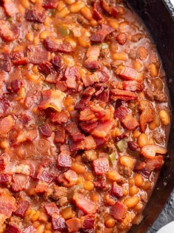 A cast iron pan with a baked bean dish topped with crispy bacon.