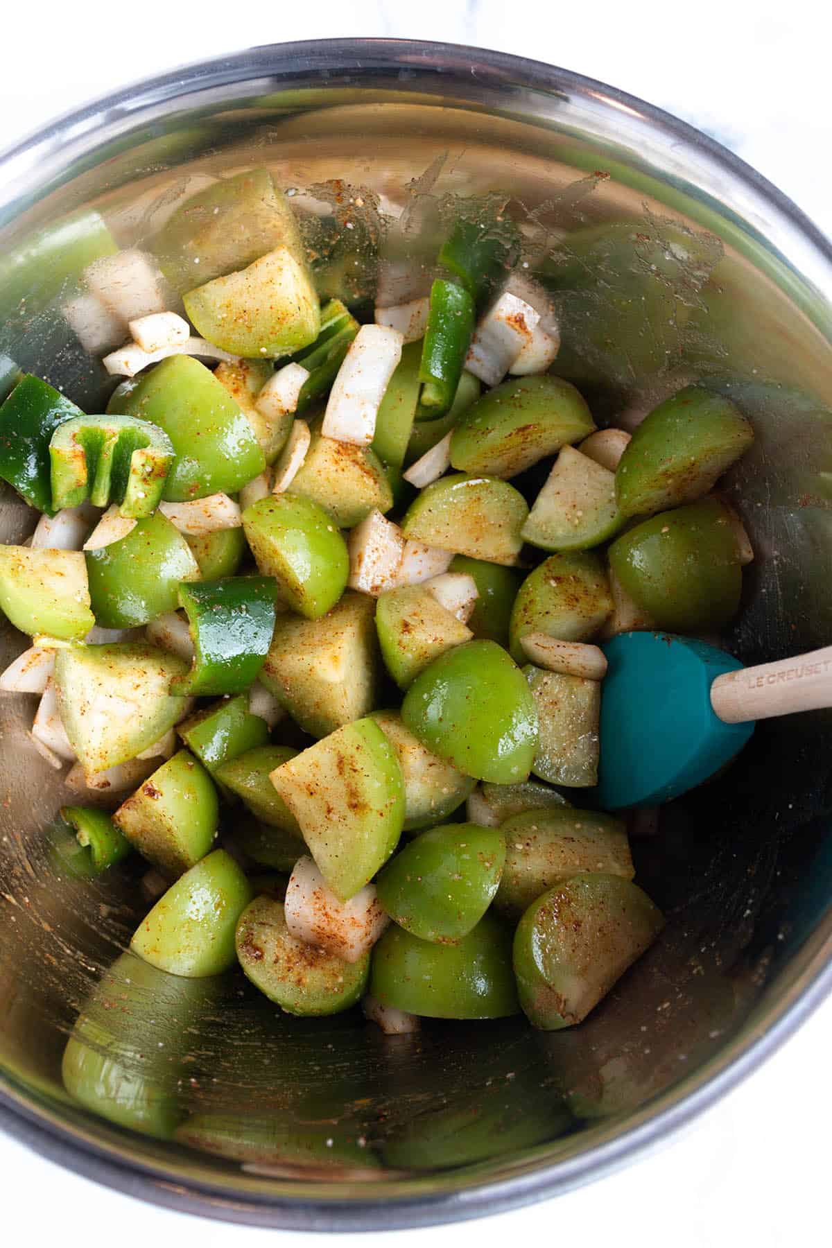 A spatula mixing up tomatillos, spices, and olive oil. 