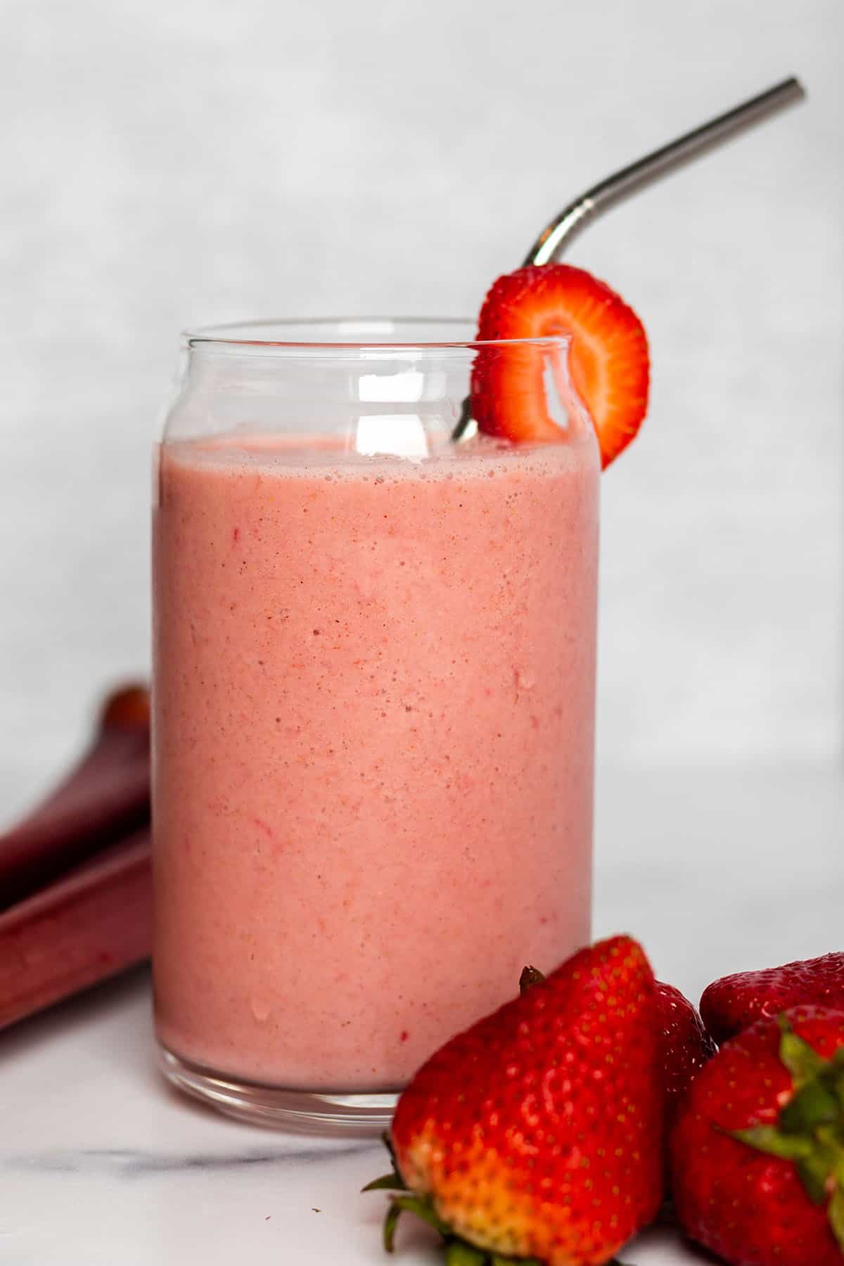 A glass with a smoothie and piles of fresh strawberries and rhubarb stalks.