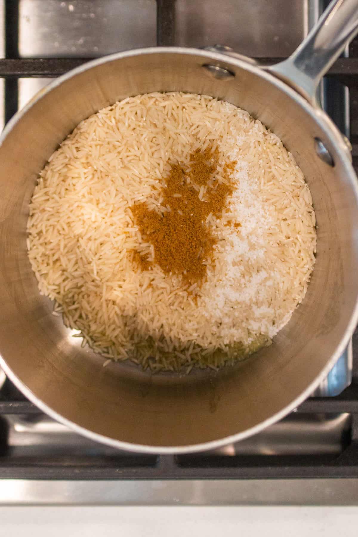 A small pot on the stove with rice, cumin and salt.