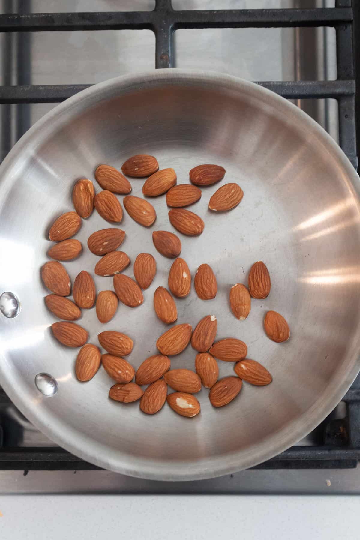 A small frying pan with almonds being toasted on the stove. 