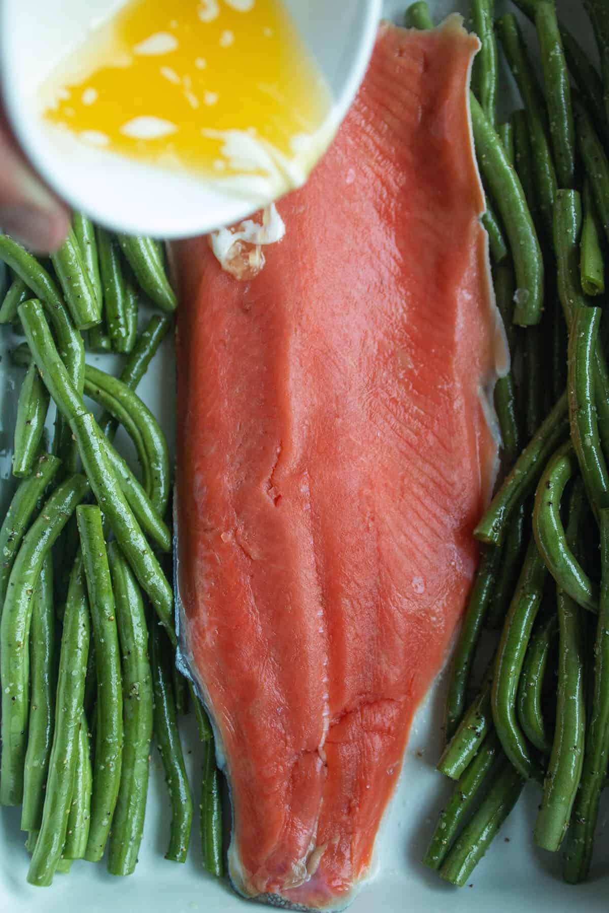 Salmon fillet with green beans and butter being drizzled on top.