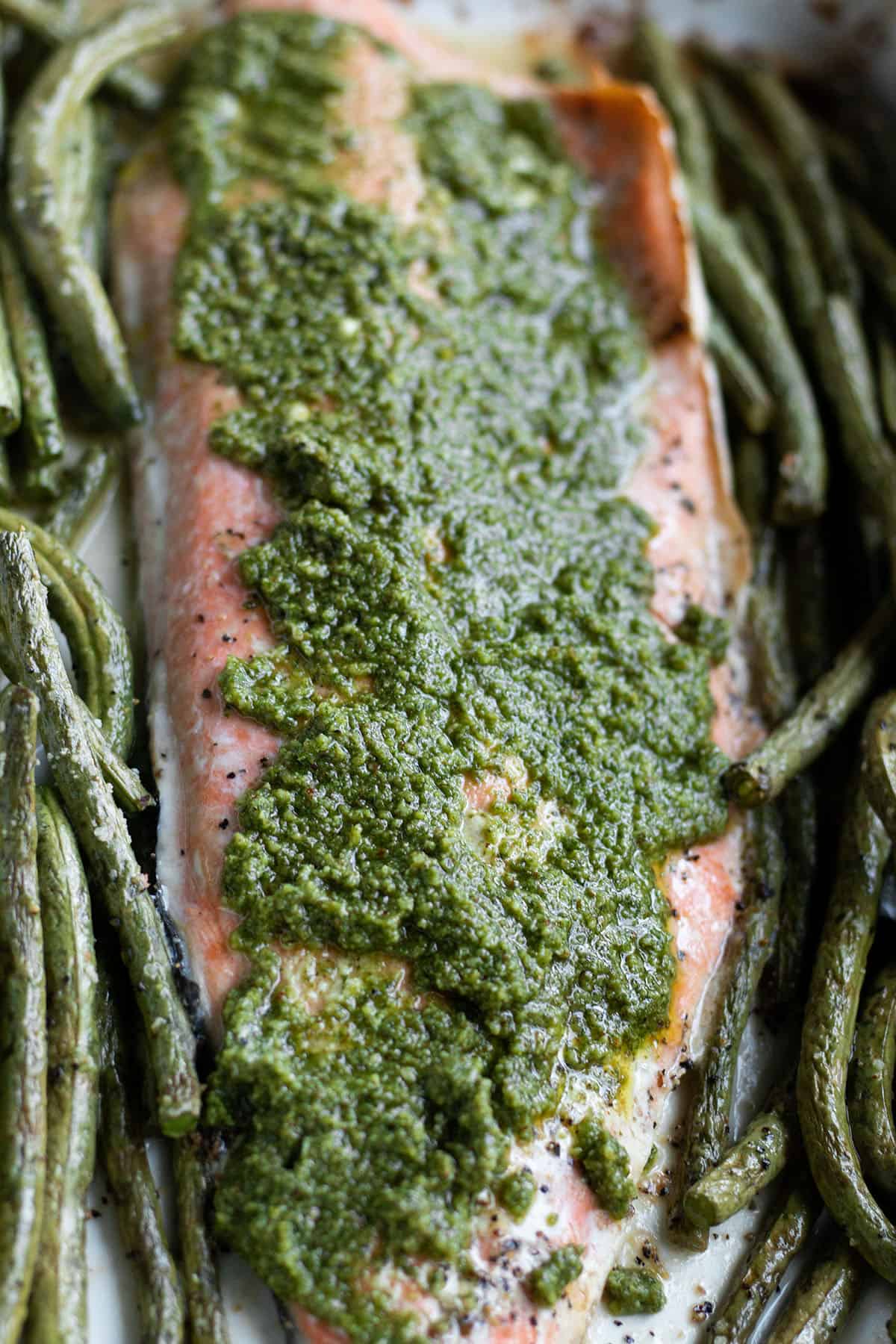 A salmon filet with fresh pesto on top with a side of green beans. 