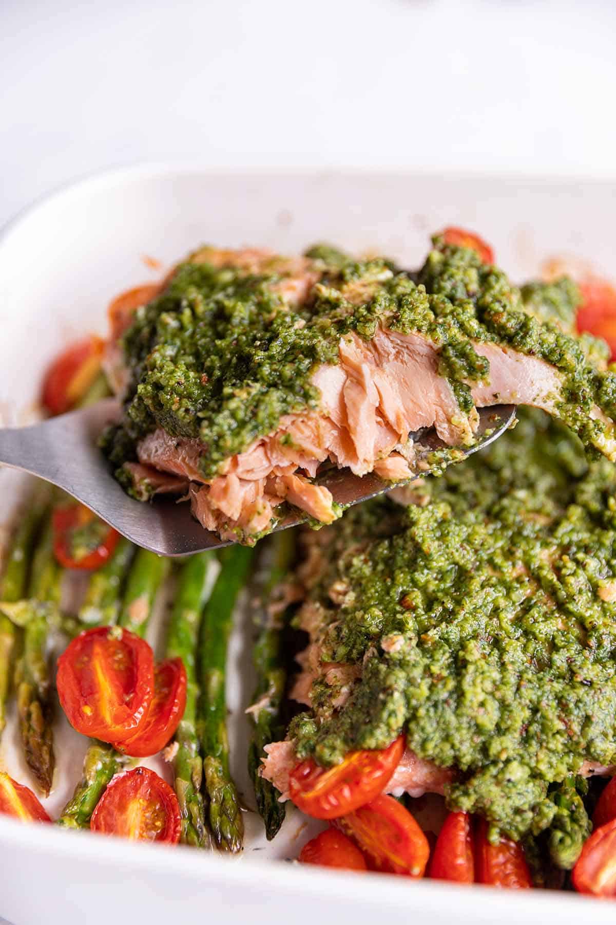 A spatula picking up a filet of salmon with pesto on top. 