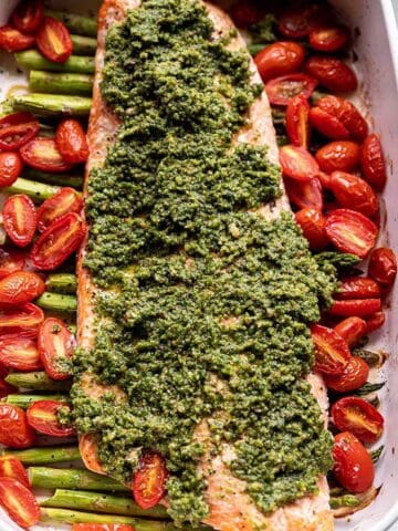 A baking dish with asparagus and salmon filet with fresh pesto on top.