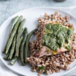 A plate with a bed of farro and baked salmon filet with pesto and a side of green beans.
