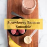 Wooden board with a smoothie, banana, frozen strawberries, protein powder, and peanut butter.