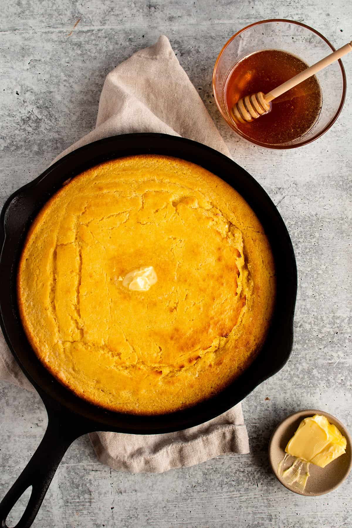 A cast iron pan with cornbread and sides of honey and butter. 