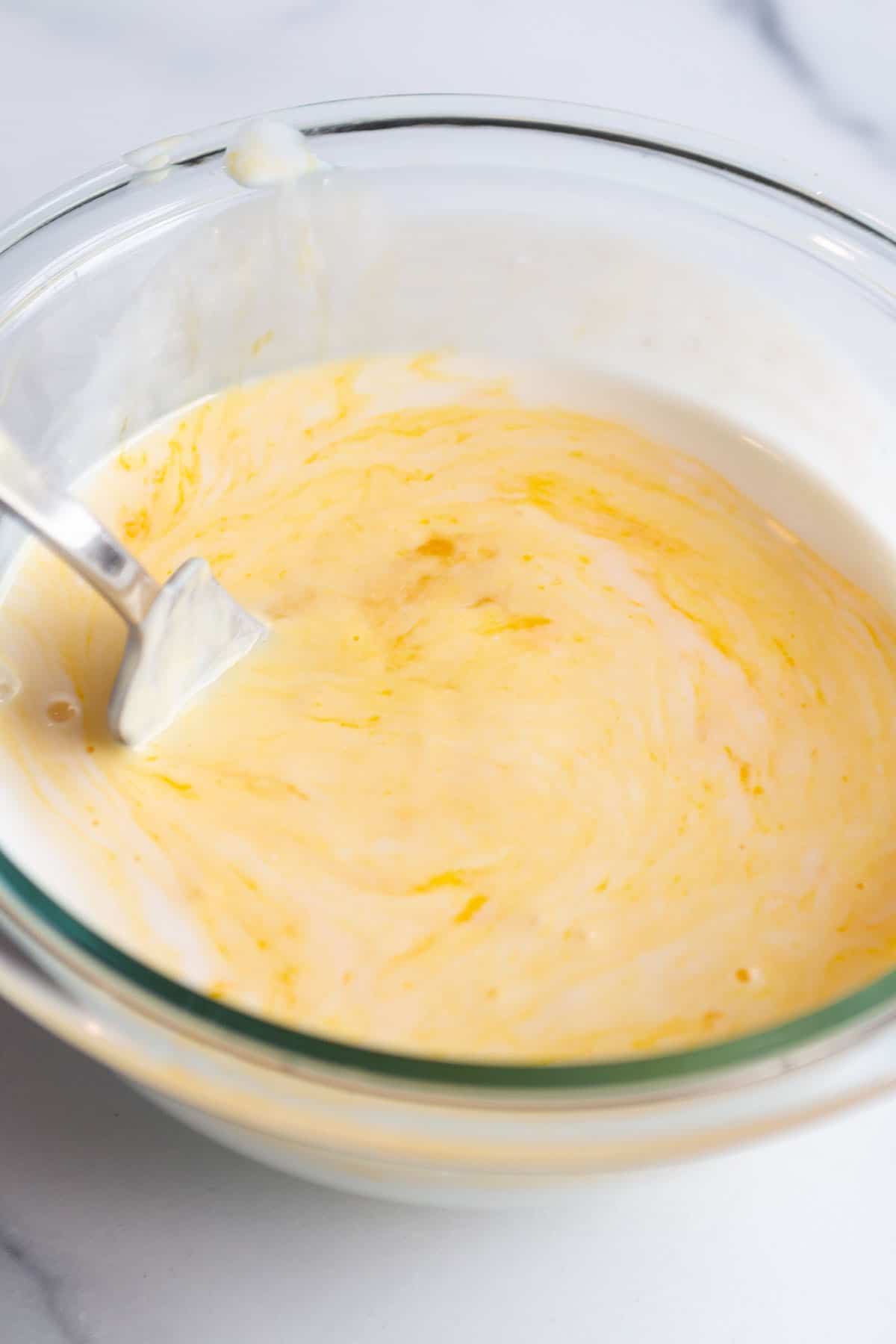 A small mixing bowl with buttermilk and eggs being whisked with a fork.
