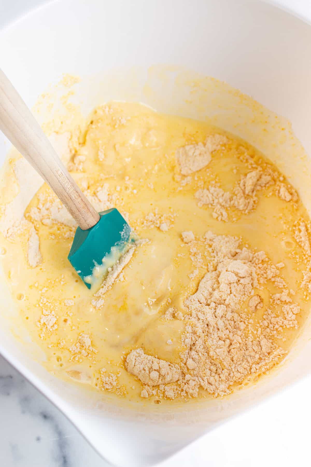 A large mixing bowl with a spatula mixing together the dry and wet ingredients. 