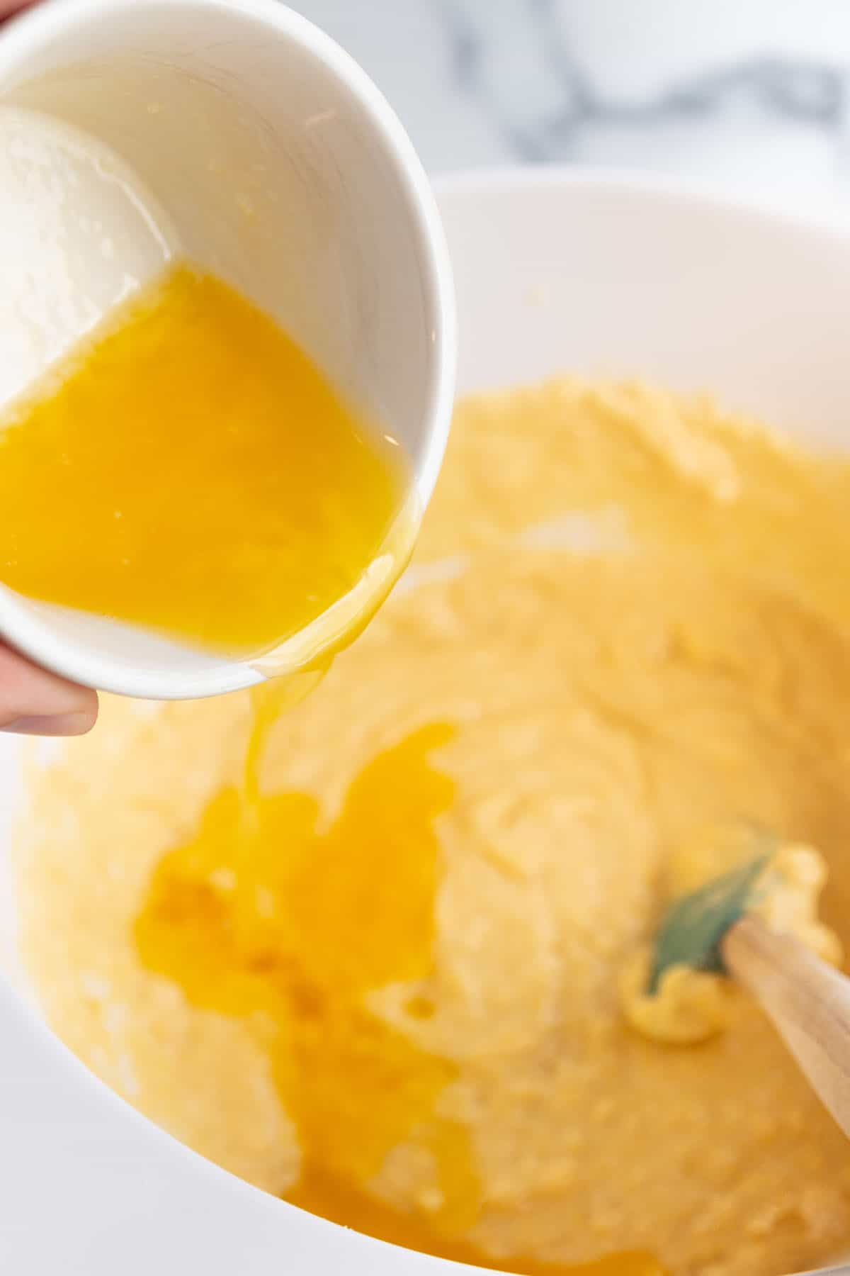 A large mixing bowl with cornbread batter with melted butter being added.