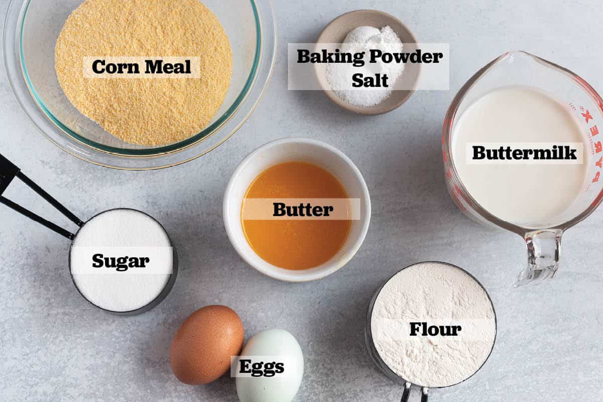 Ingredients laid out for cornbread. Buttermilk, flour, cornmeal, eggs, sugar, butter, baking powder, and salt.