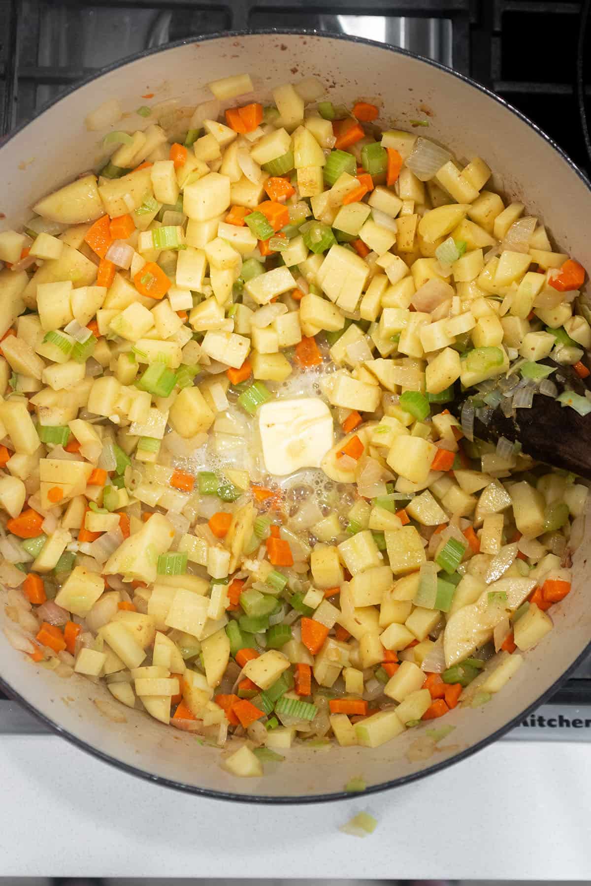 Large Dutch Oven with veggies sautéing and butter being melted.