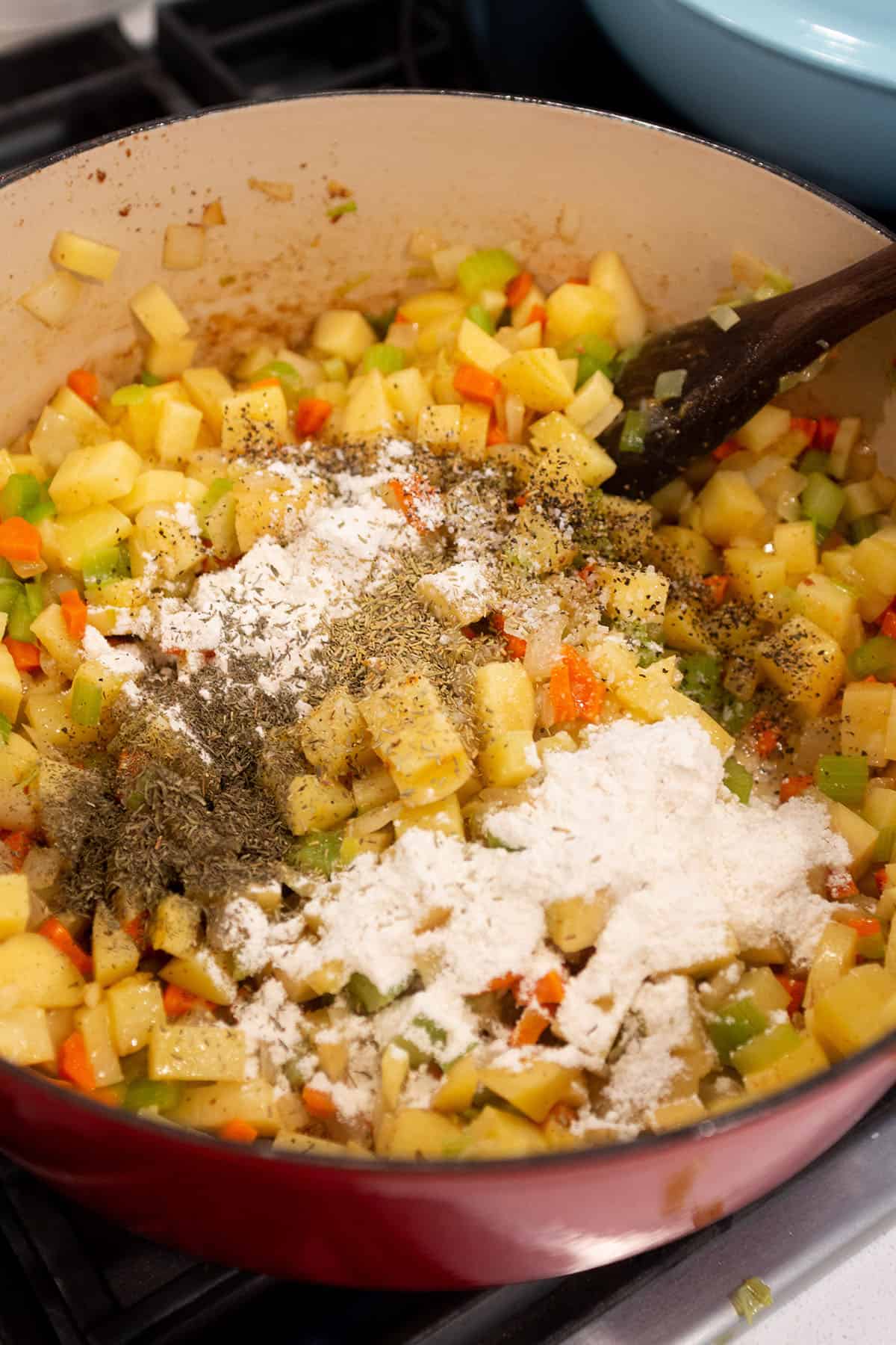 Large Dutch Oven with sautéed veggies with flour and seasonings being added. 