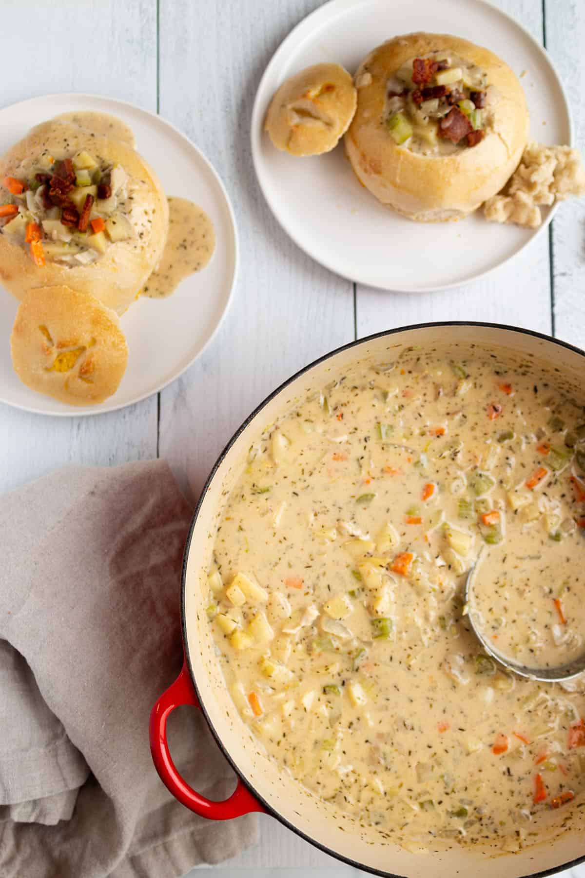A large soup pot with a creamy clam chowder and two plates with sourdough bread bowls.