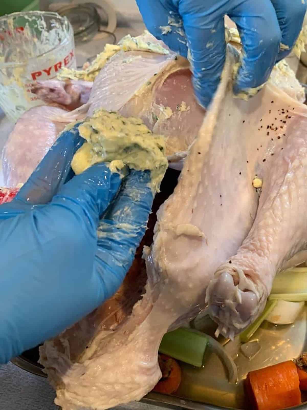 Two hands stuffing a butter compound under the skin of a turkey. 