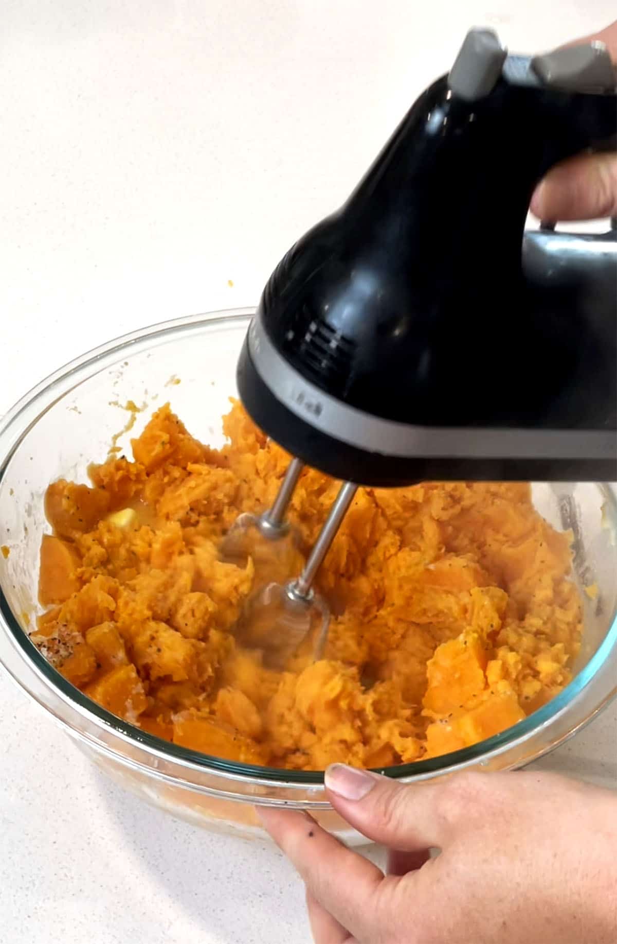 A mixing bowl with sweet potatoes, butter and a hand mixer creaming everything together. 