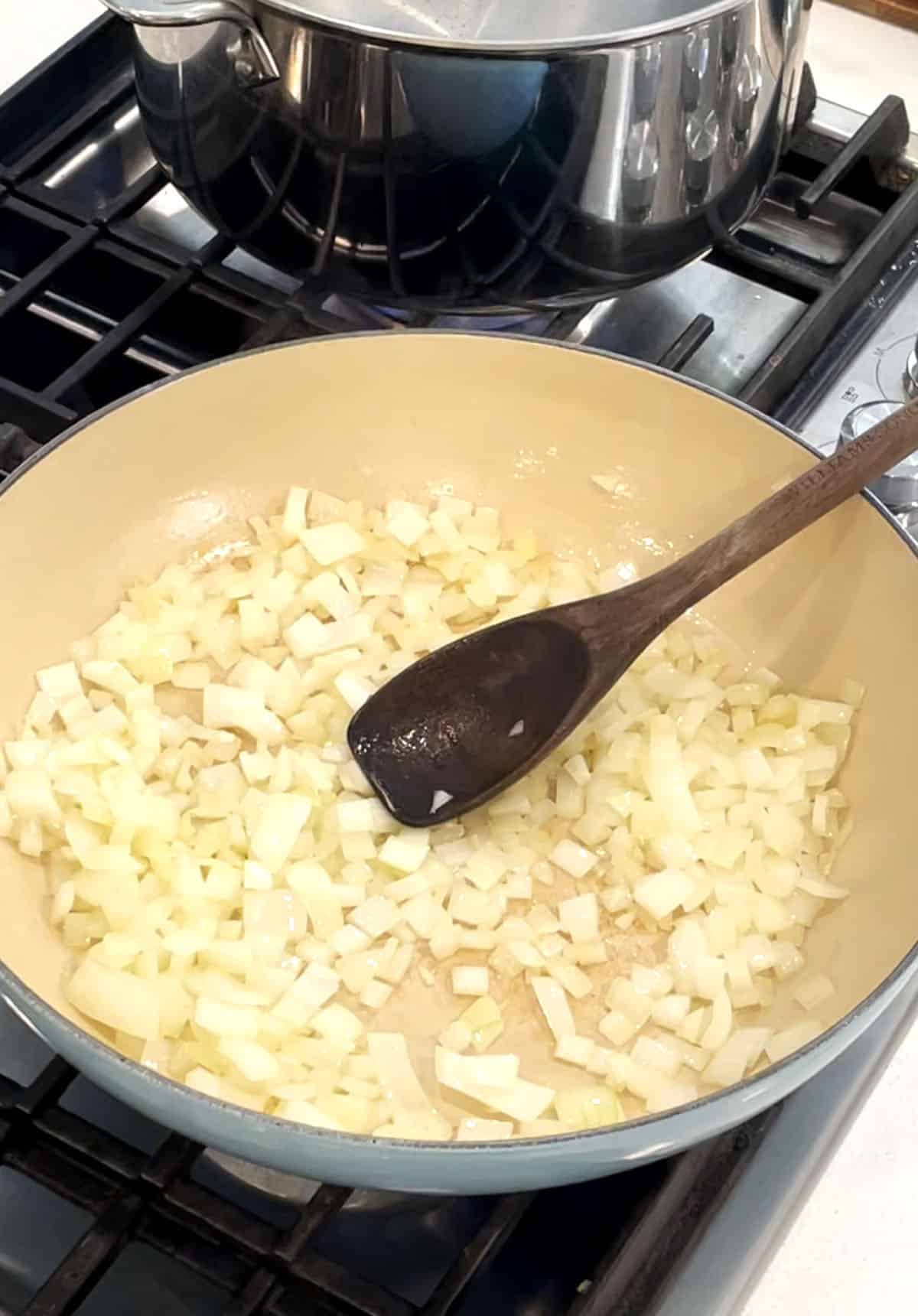 Large skillet with sautéed onions and wood spoon. 