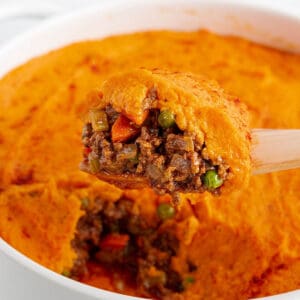 Circle baking dish with a layer of ground beef mix with a sweet potato mash on top. Spatula scooping out a serving.