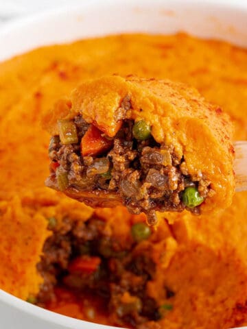 Circle baking dish with a layer of ground beef mix with a sweet potato mash on top. Spatula scooping out a serving.