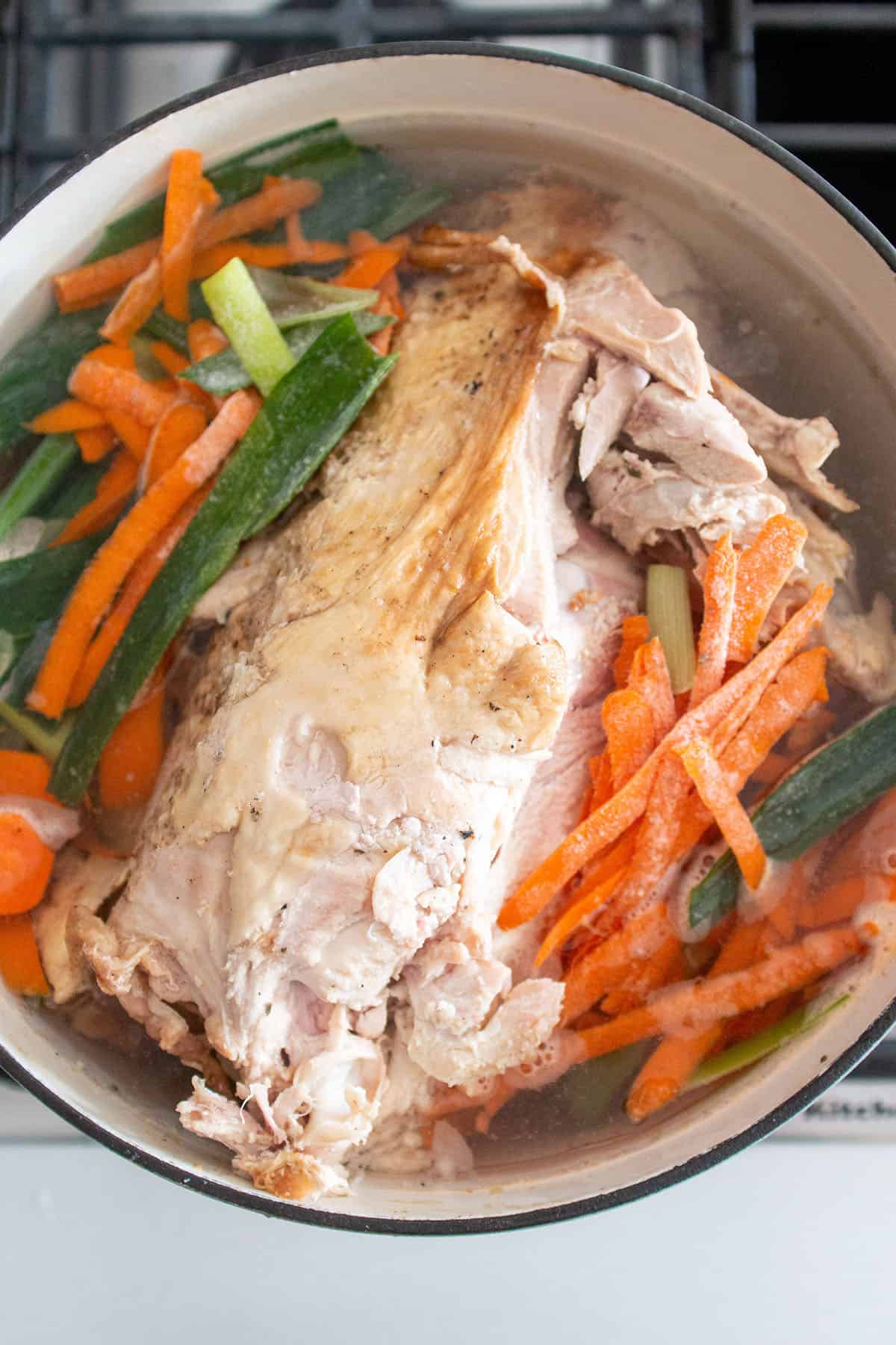 Large Dutch Oven on the stove with a turkey carcass, veggies scraps and water.