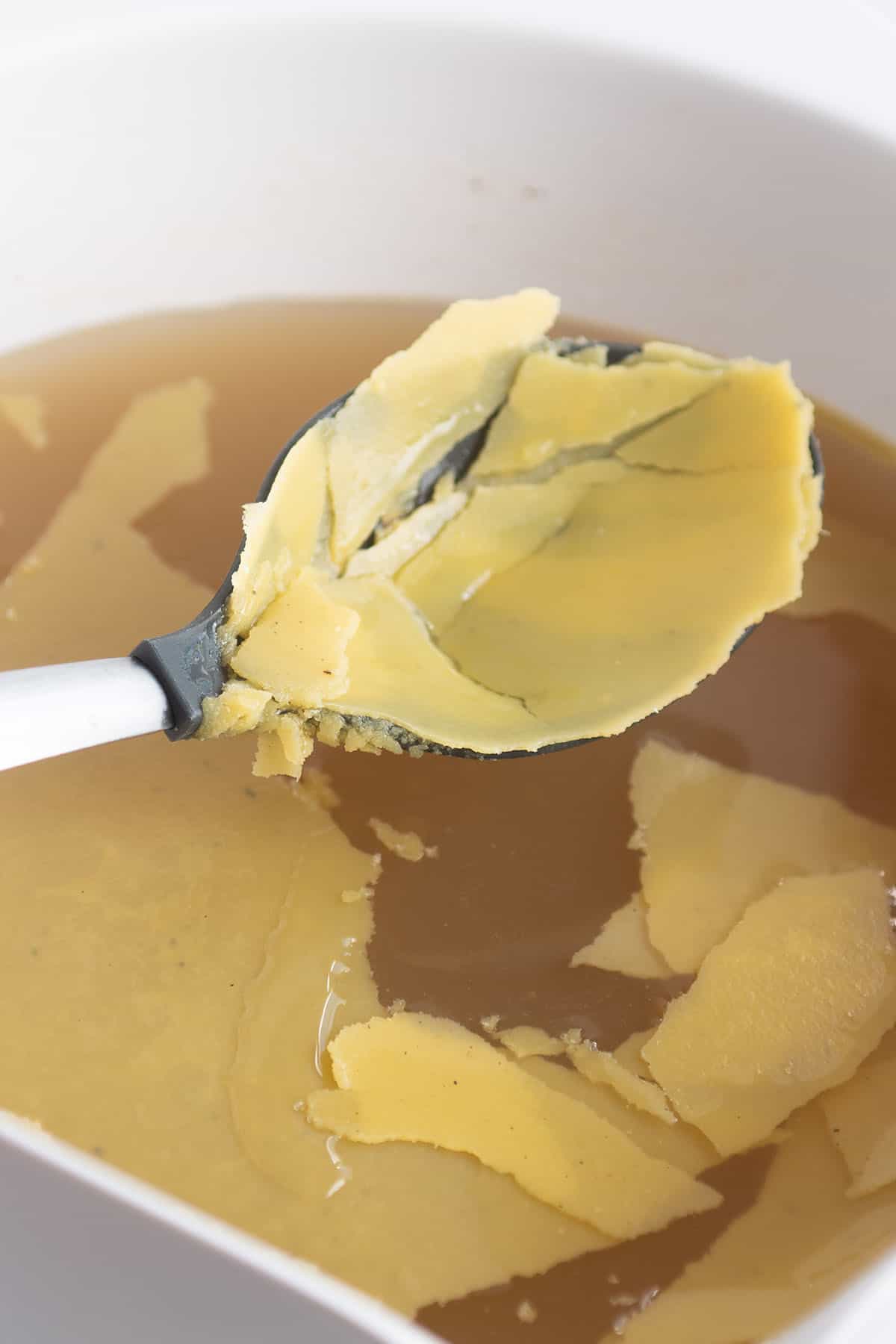 A slotted spoon scooping out fat that has become solid in a homemade broth.